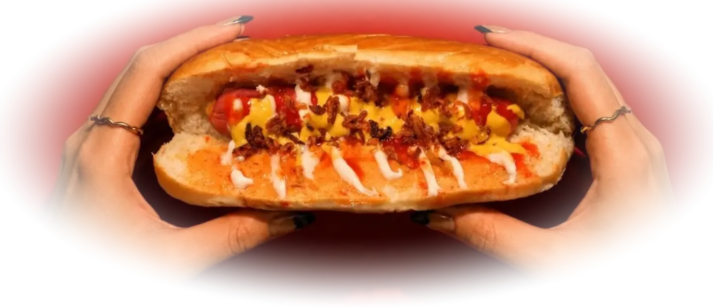 Kırmızı fonda iki elle tutulan, soslu hot dog
