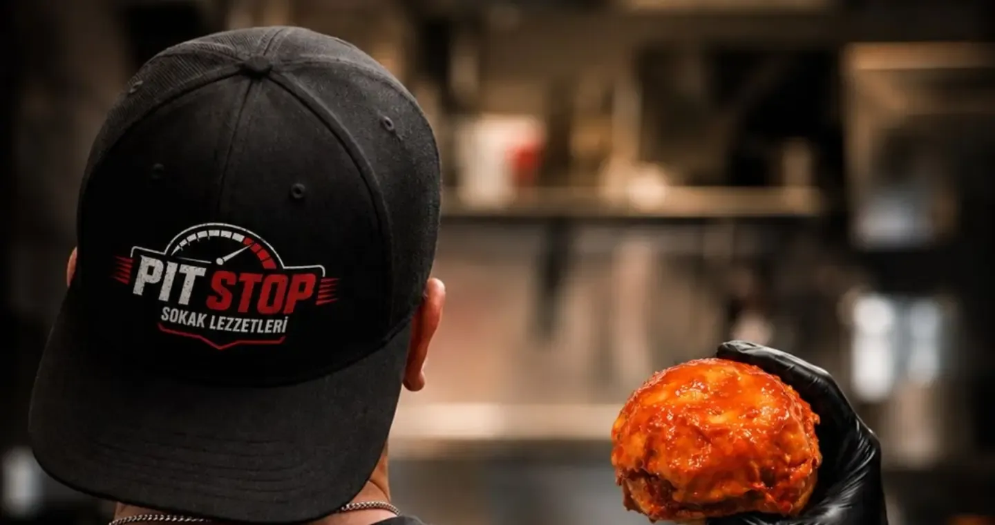 Arkası dönük, Pit Stop şapkalı usta; eldivenli elinde ıslak hamburger